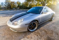 A silver 1999 Porsche Carrera with custom hood and Carrera stripes made of carbon fiber vinyl.