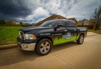 Partial vehicle wrap for Lawns Plus. Logo sitting in the grass on a black RAM D-1500.