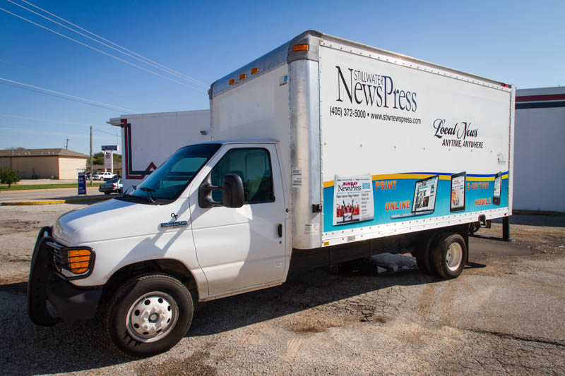A white box truck with a partial vehicle wrap for Stillwater News Press. Front three quarters view.