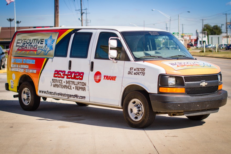 Front three quarters view of a bright red and yellow vehicle wrap on a Chevrolet Van for Executive Heat and Air.